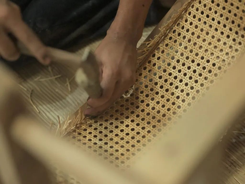 Hand-weaving cane onto a chair frame at Wood Factory